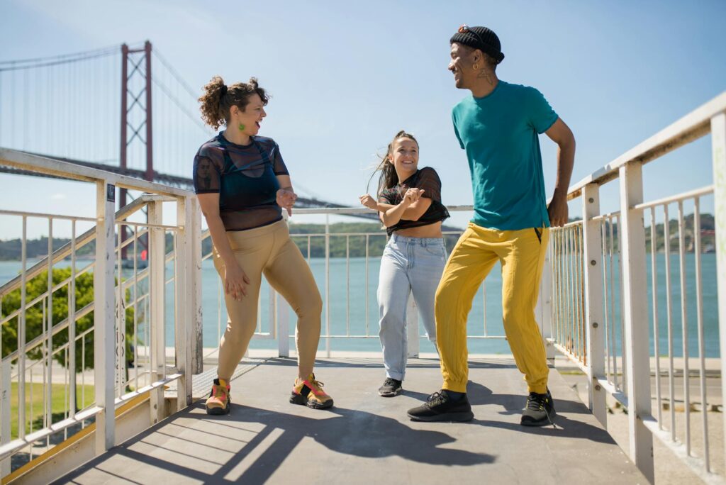 Three friends dancing joyfully outdoors in Lisbon with the iconic bridge in the background.